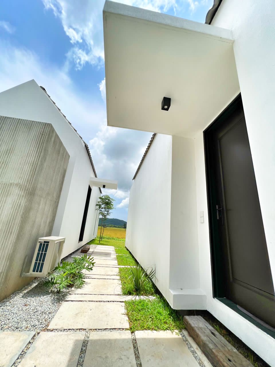 Ezu Isle Langkawi villa with pool: stone path between the white A-frame suites, a suite door, padi fields and hills at the end