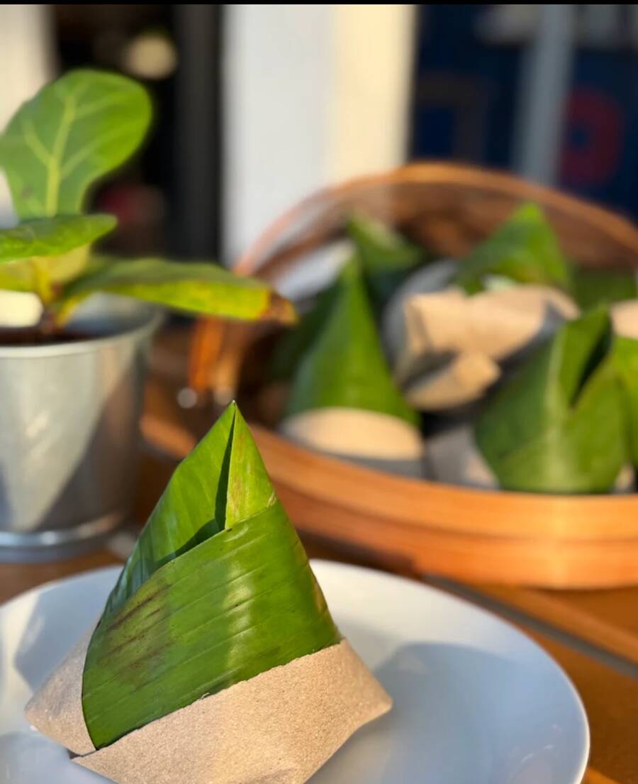 Nasi lemak bungkus — banana leaf pyramids on a plate, with a basket of more behind